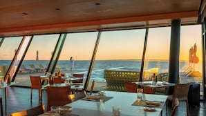 A restaurant with tables set for dining, large windows offering a view of the ocean, and outdoor seating with umbrellas. - Playa Vik Jose Ignacio (José Ignacio)