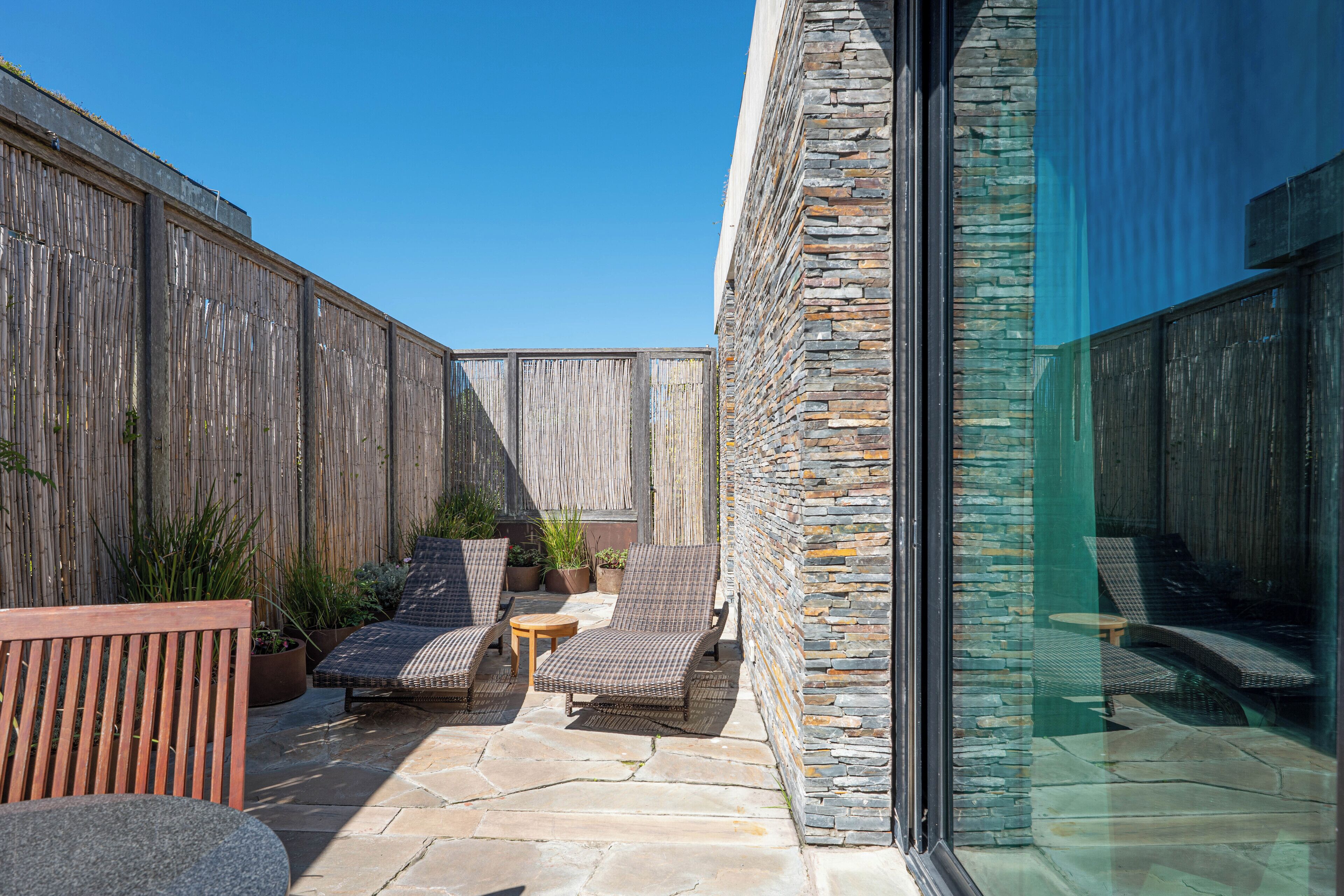 A patio with stone flooring, wicker furniture, and potted plants.