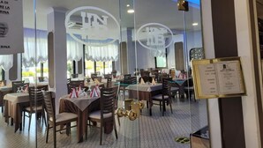 Un restaurant avec de nombreuses tables et chaises, un menu affiché sur un panneau à droite et un grand logo sur le mur.