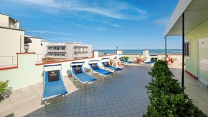Une terrasse sur le toit avec des chaises longues, une vue sur la mer et un immeuble doté d’un balcon.