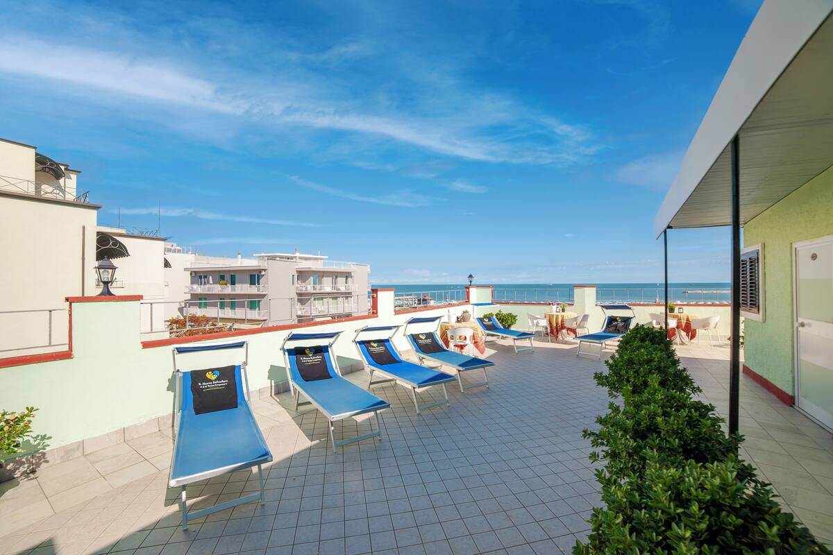 Eine Dachterrasse mit Liegestühlen, Blick auf das Meer und ein Gebäude mit Balkon.
