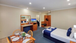 Ett hotellrum med en säng, ett skrivbord med en dator, en tv, en matplats med ett bord dukat för två personer och ett litet pentry.