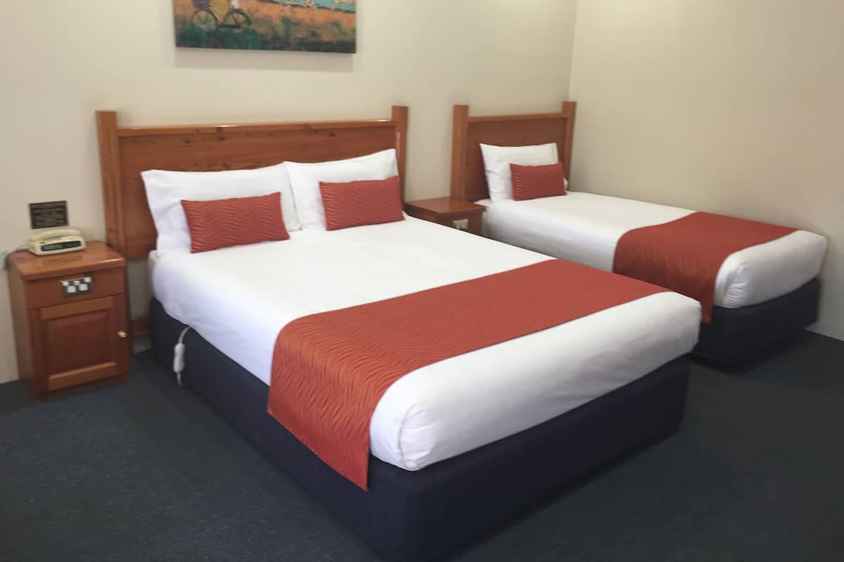 A hotel room with two single beds, each with white linens and red accents, a wooden headboard, a nightstand with a telephone, and a painting of giraffes on the wall.