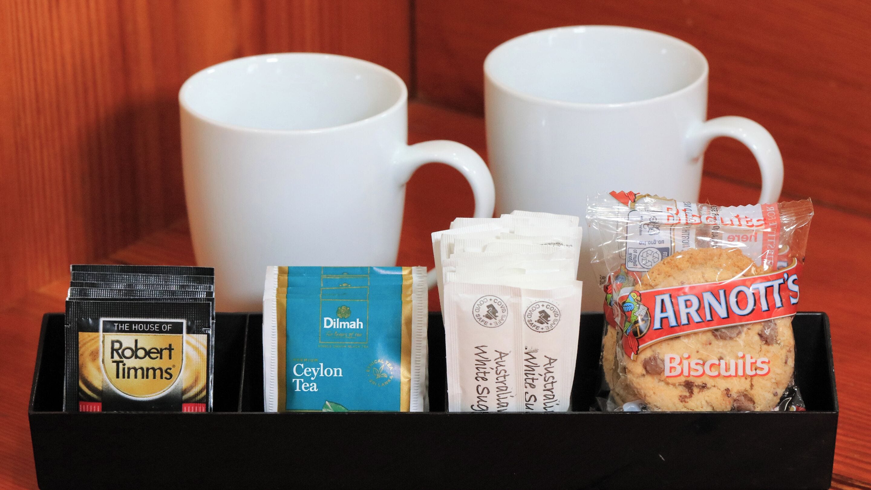 Uma bandeja com uma caneca de café, um sachê de chá, um pacote de biscoitos e um saquinho de chá.