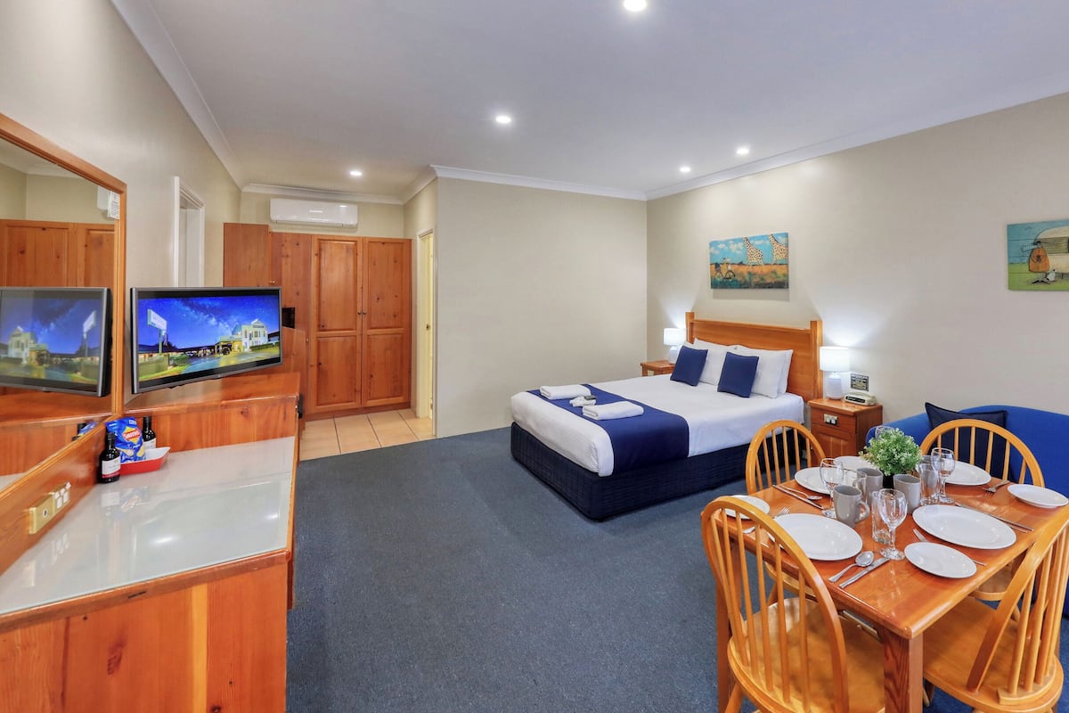 A hotel room with a bed, a TV, a dining table with chairs, and a blue sofa.