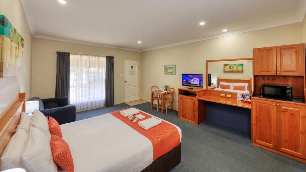 A hotel room with a bed, desk, television, and a microwave.