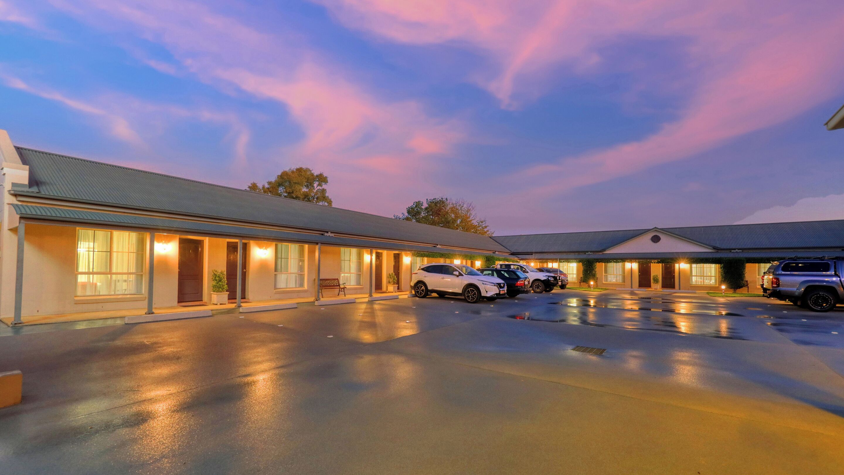 A motel with a row of rooms, a parking lot, and a building with a flat roof.