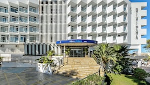 Un hôtel moderne à la façade géométrique originale, doté d’une entrée imposante avec des marches et d’une enseigne indiquant qu’il s’agit du « Vibra Riviera Hotel ».