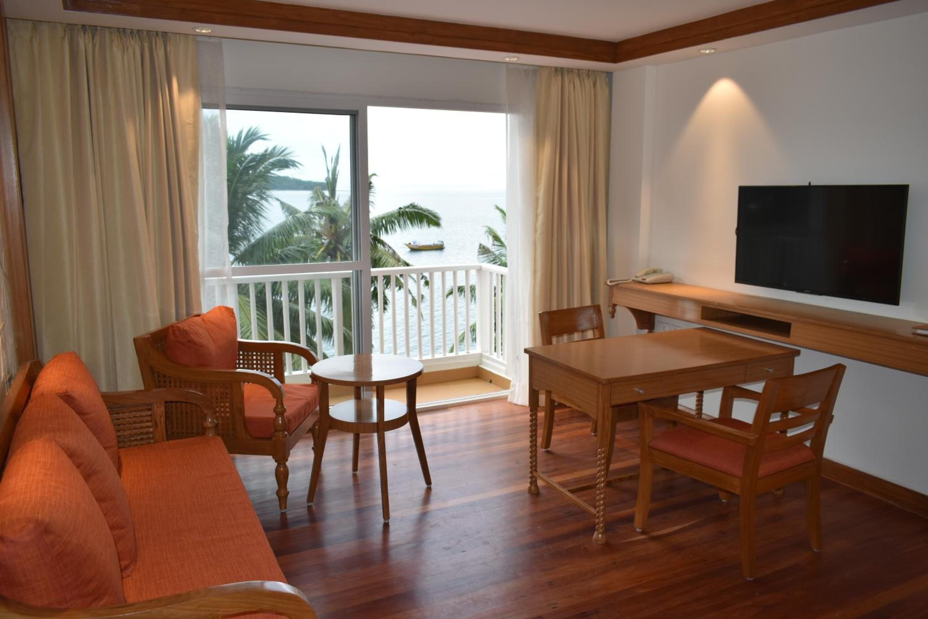 Une chambre avec balcon, des meubles en bois, une télévision et vue sur la mer.