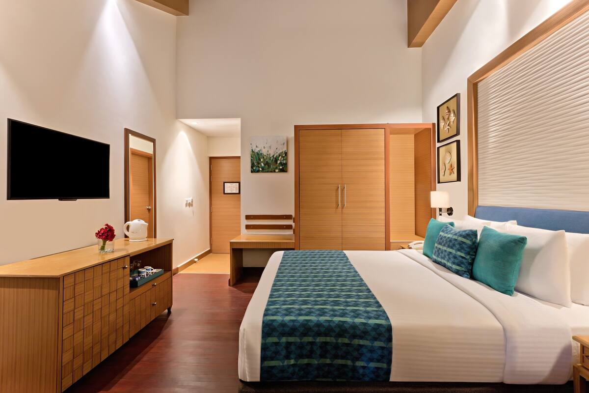Ein modernes Hotelzimmer mit einem großen Bett, einem Holzschrank, einem Fernseher und einem Schreibtisch mit Stuhl.