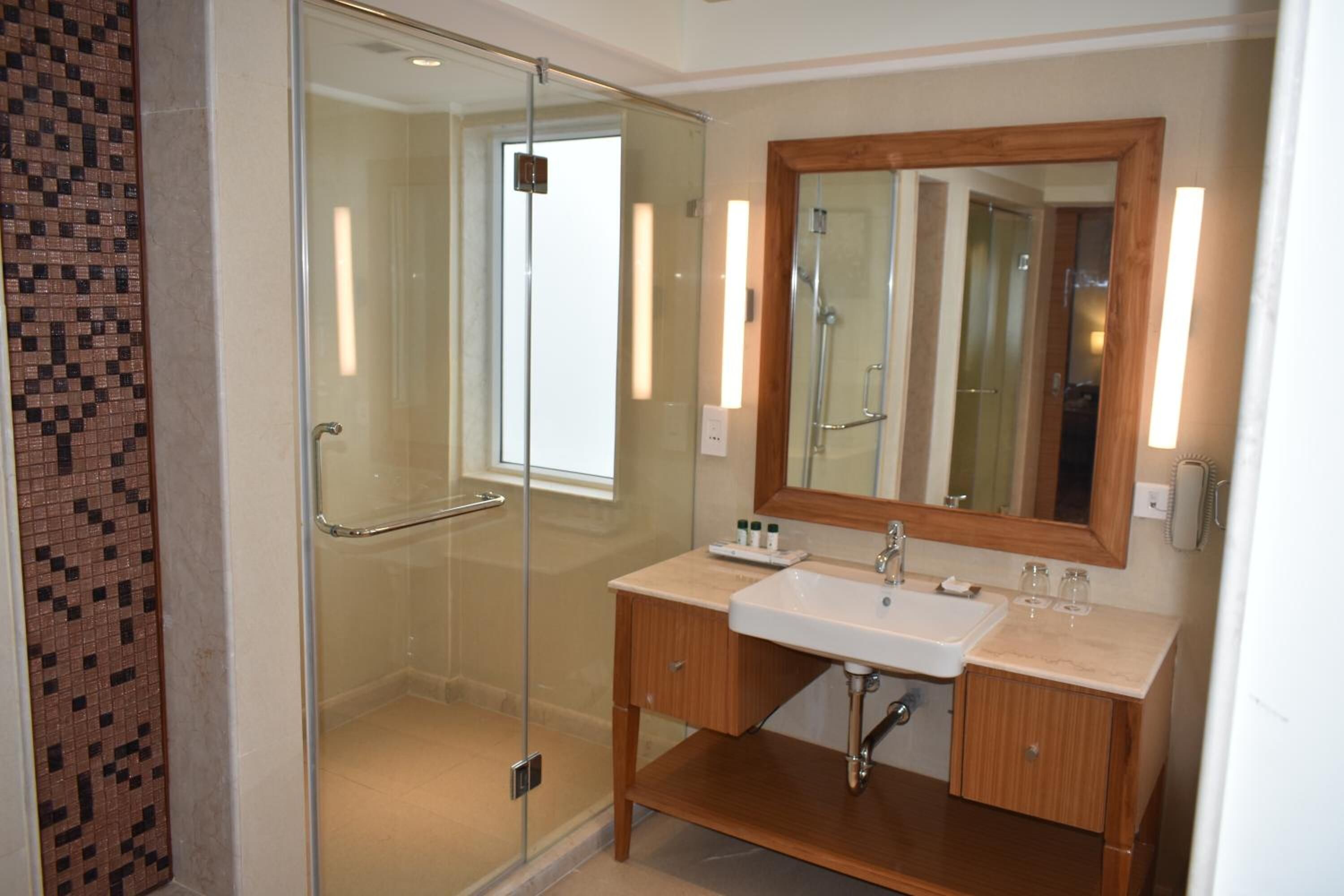 A modern bathroom with a glass-enclosed shower, a wooden vanity with a white sink, and a large mirror.
