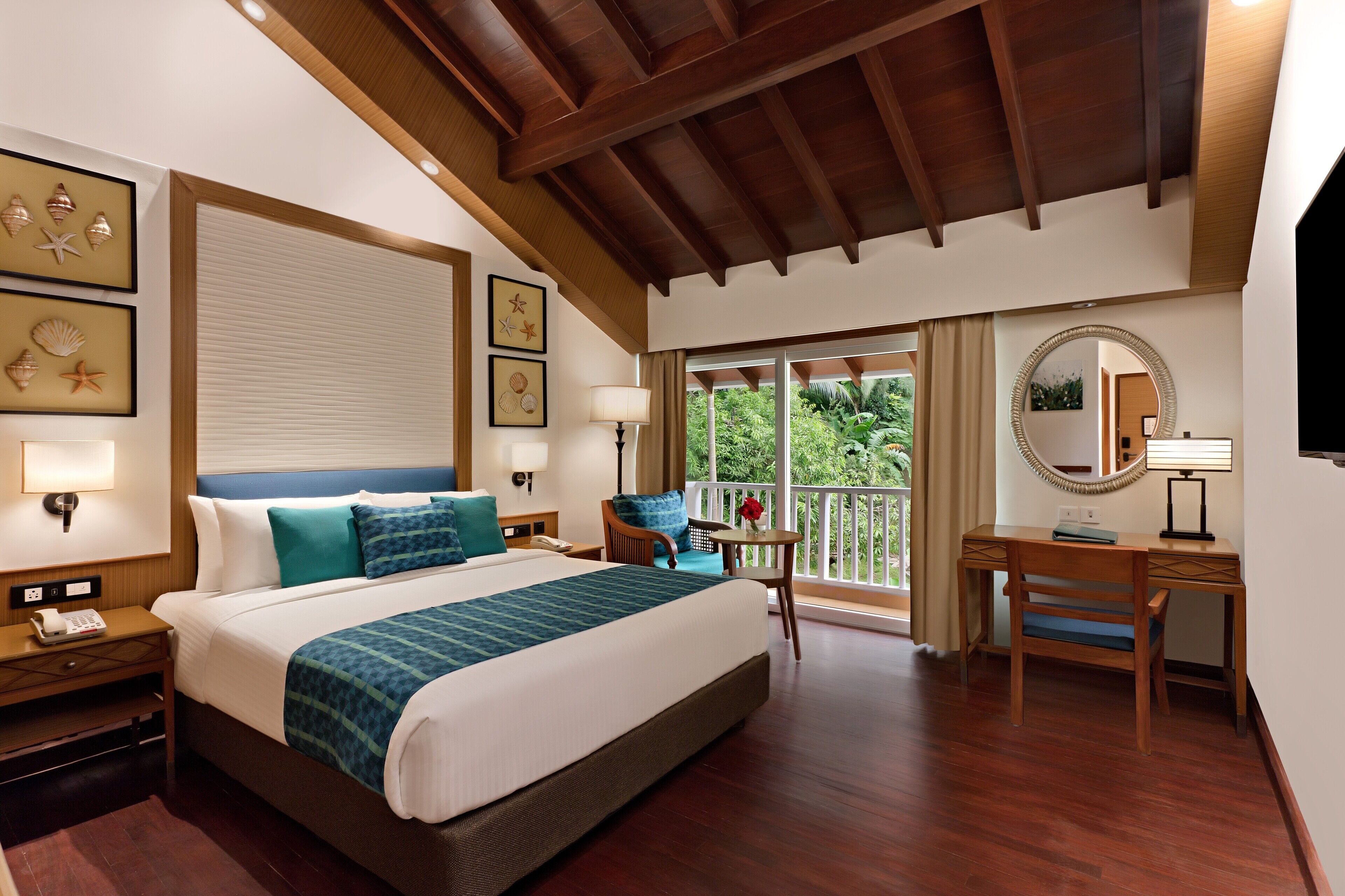 A hotel room with a large bed, a desk, a chair, a nightstand, a lamp, and framed pictures on the wall.