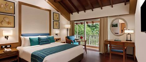 A hotel room with a large bed, a desk, a chair, a nightstand, a lamp, and framed pictures on the wall.