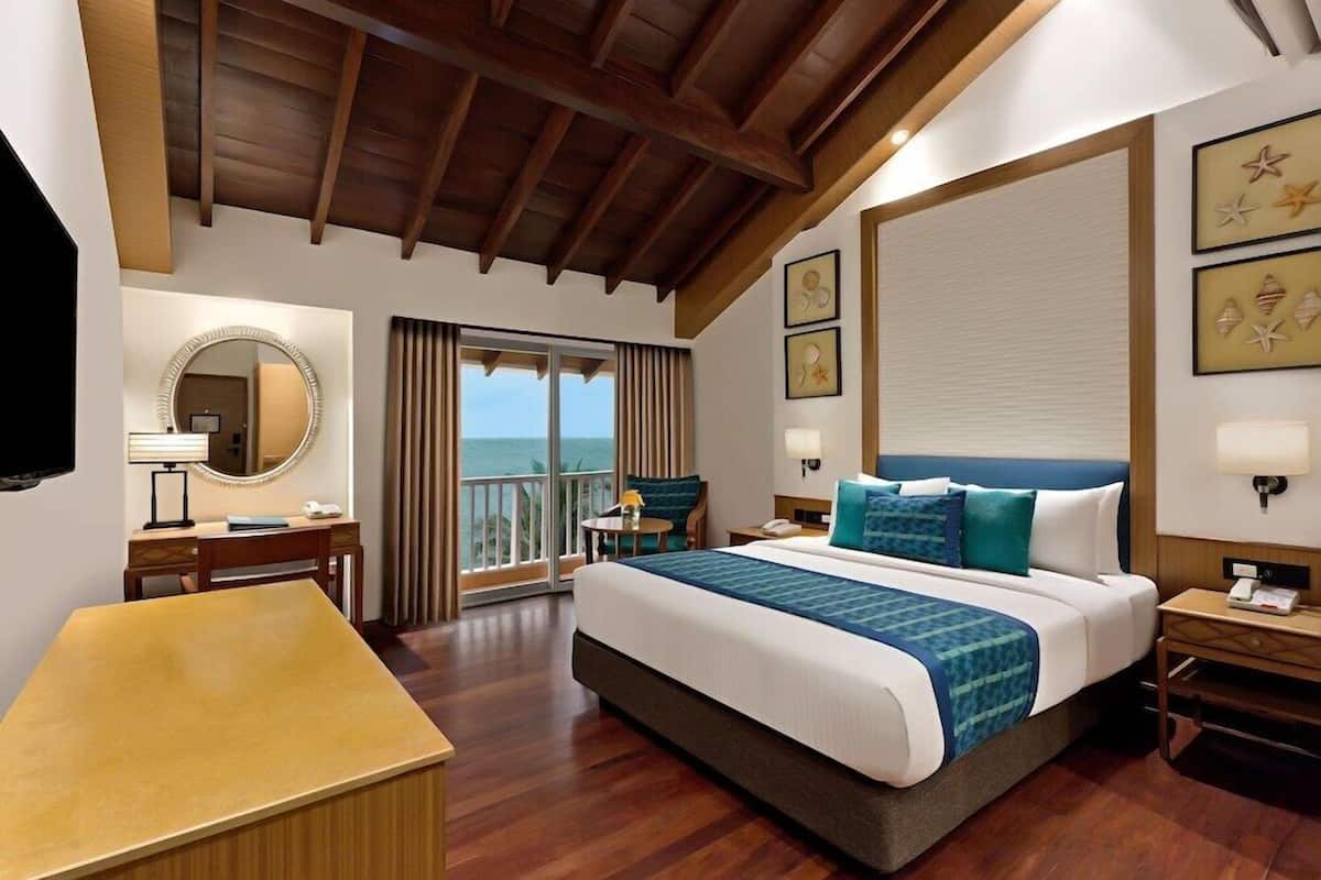 Ein Hotelzimmer mit einem großen Bett, einem Schreibtisch, einem Sessel und einem runden Spiegel, mit Blick auf das Meer.