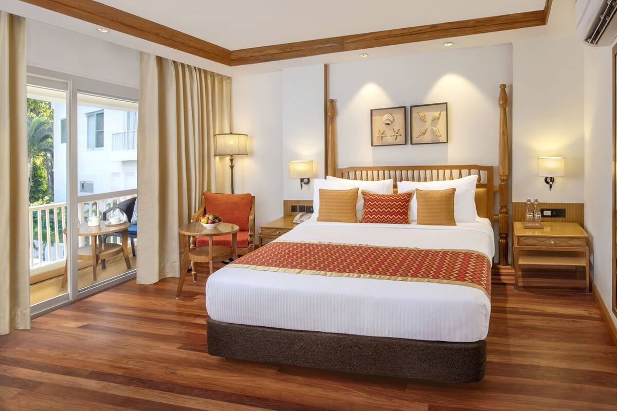 Ein Hotelzimmer mit einem großen Bett, einem Balkon, einem Sessel und einem Tisch mit Obstschale.