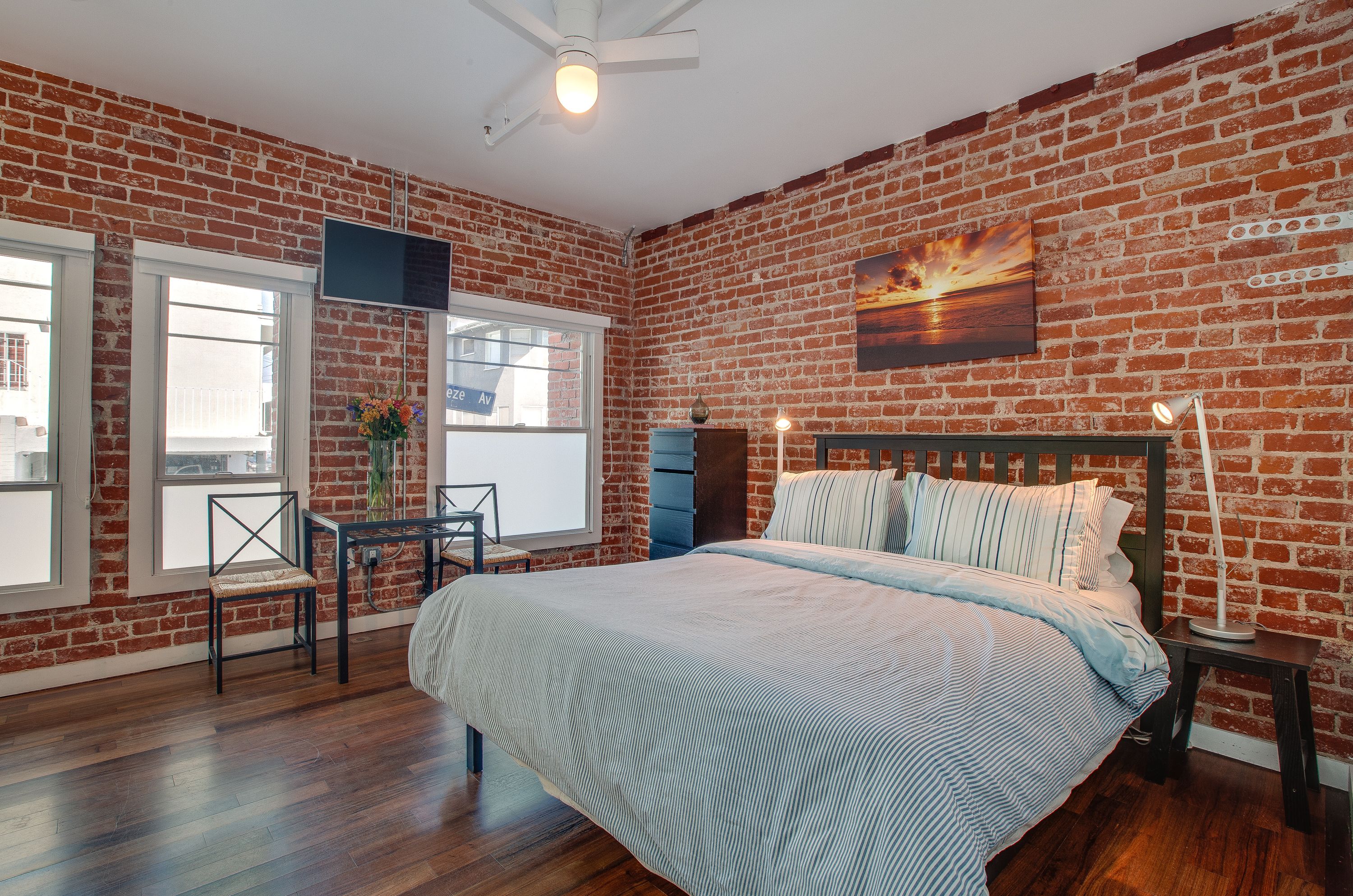 Une chambre avec un mur en briques, un lit, une télévision et une fenêtre.