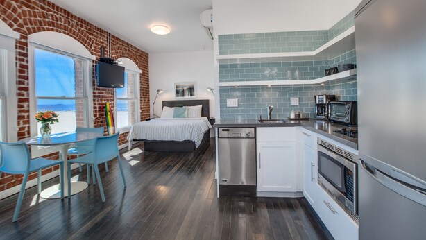 A modern kitchen with a dishwasher, oven, and microwave. There is a bed with a view of the ocean. - Venice Breeze Suites (Venice)