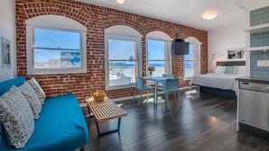 Una habitación moderna con pared de ladrillo, ventanas grandes, cama, zona de comedor y cocina.