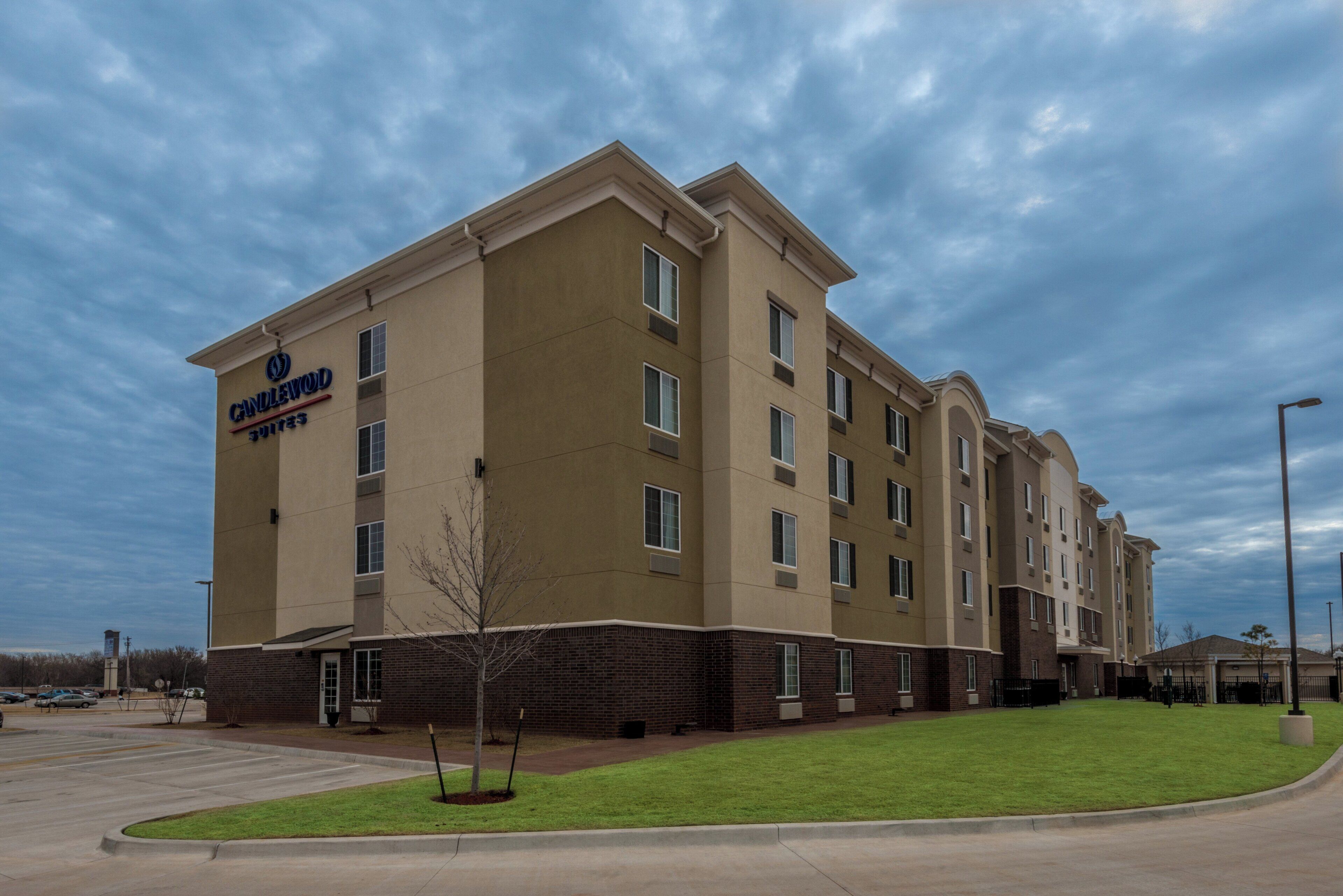 Um hotel de vários andares com telhado plano, uma placa da Candlewood Suites e um estacionamento em primeiro plano.