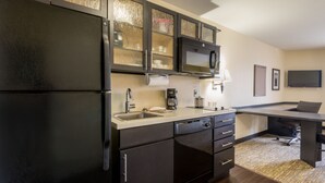 A modern kitchen with black cabinets, a stainless steel refrigerator, a microwave, and a sink.