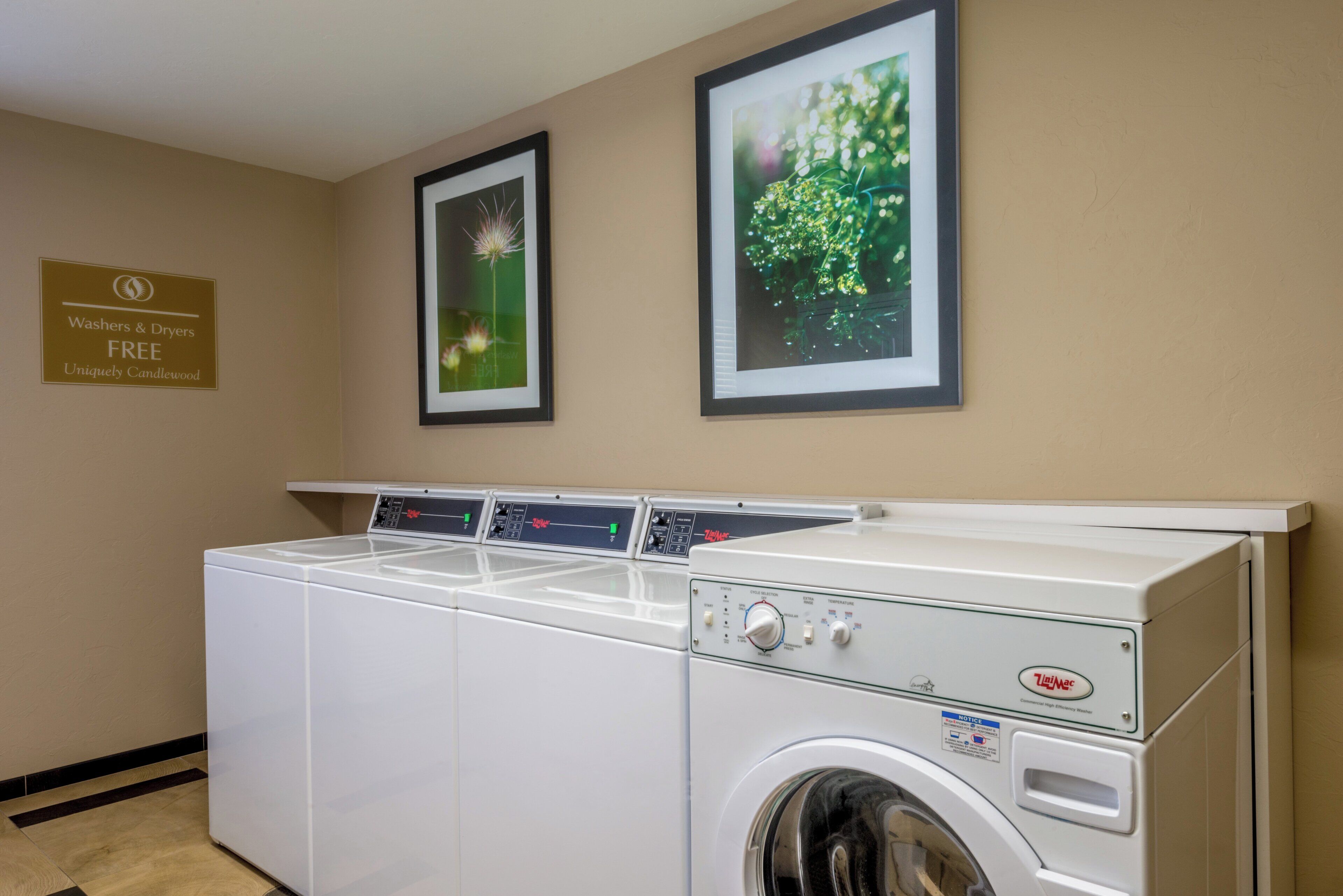 A laundry area with a front-loading washer and dryer, a sign offering free washers and dryers, and two framed pictures on the wall.
