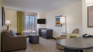 A hotel room with a sofa, armchair, desk, and a flat-screen TV.