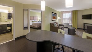 Habitación de hotel con cama, zona de estar con sofá y sillones, mesa de comedor, televisor de pantalla plana y baño con espejo y lavamanos.