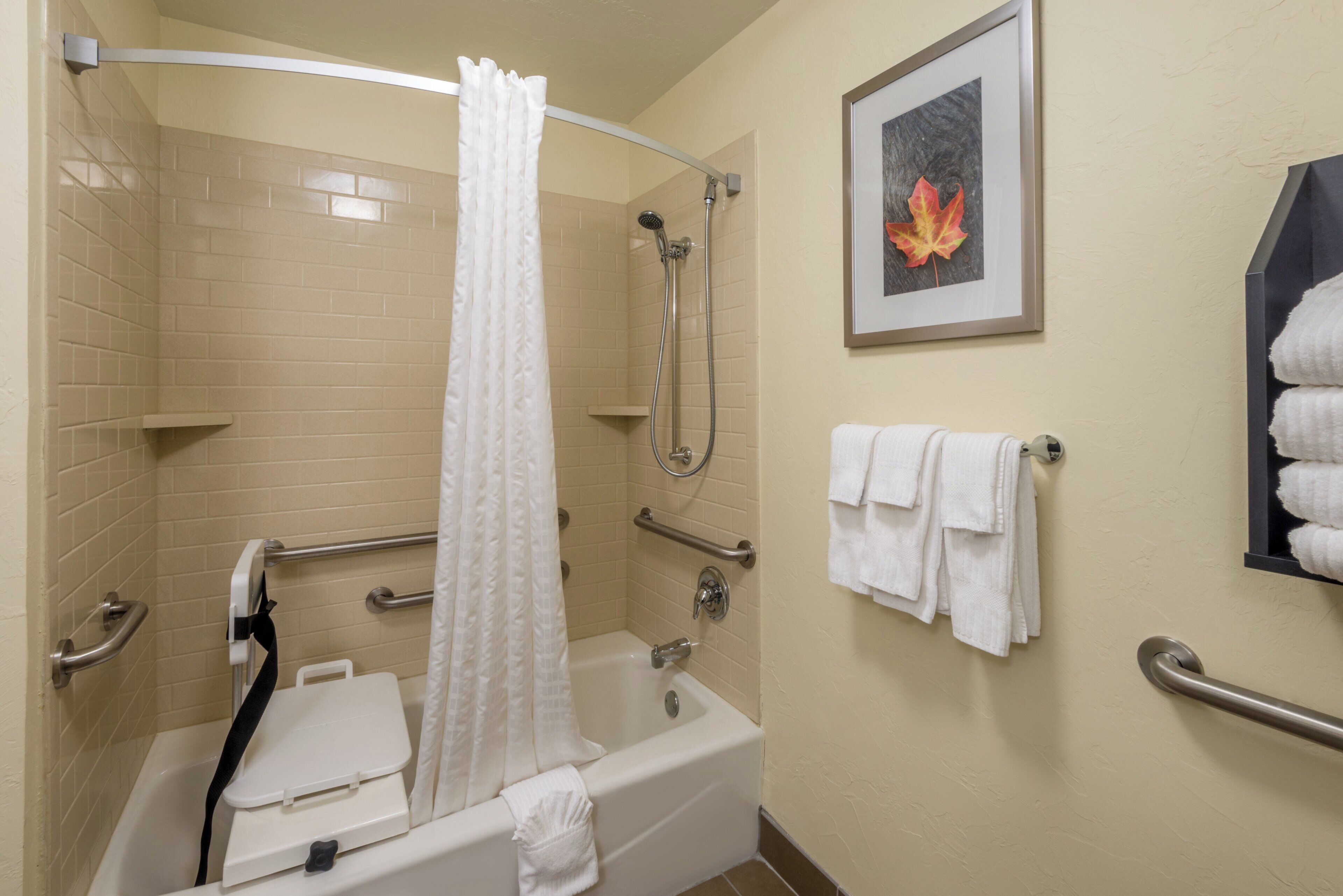 A bathroom with a bathtub, shower, and handrails.