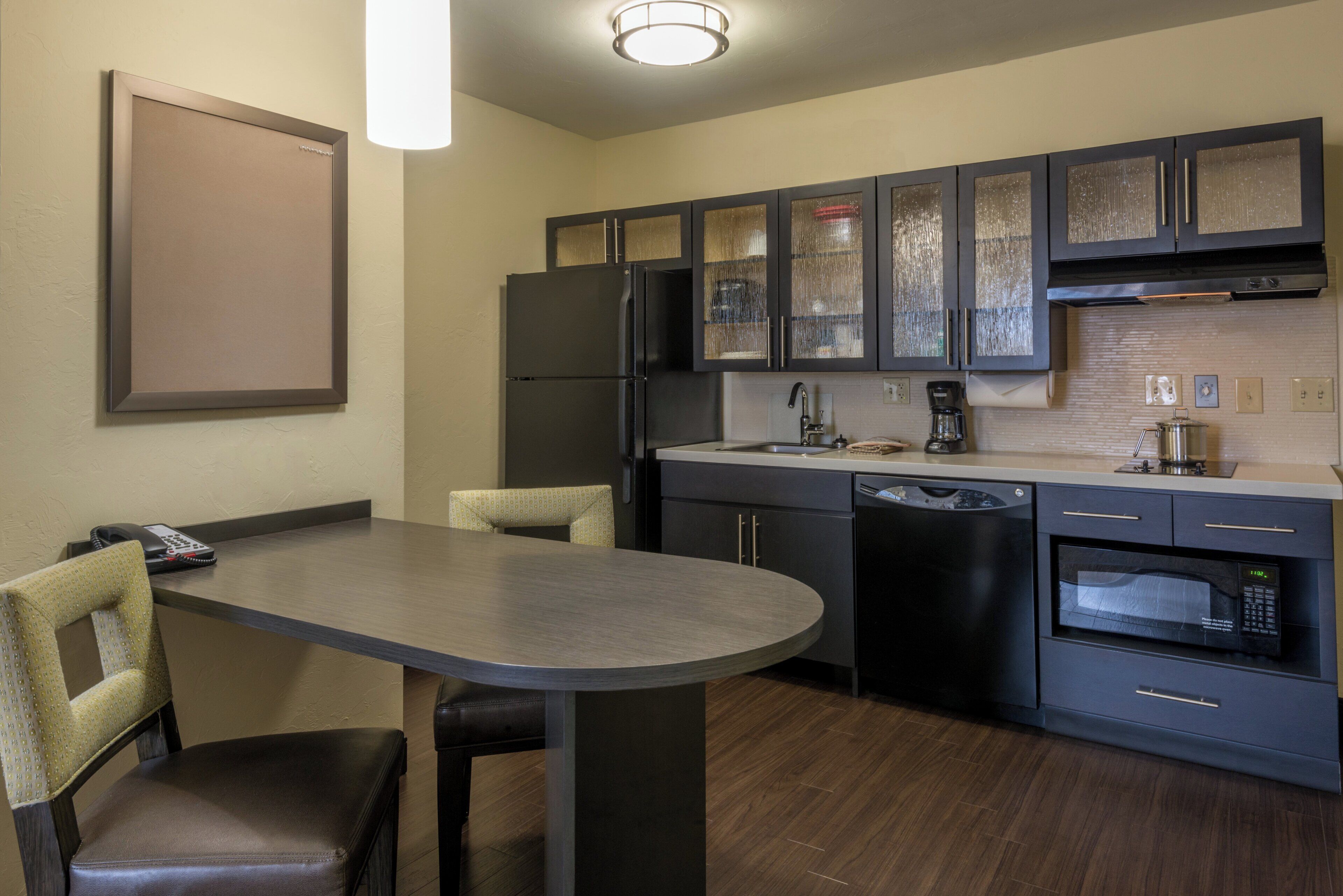 Una cocina moderna con armarios oscuros, horno empotrado y una mesa de comedor con sillas.