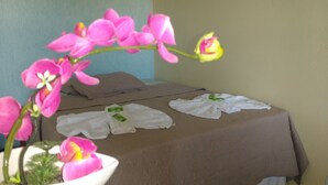 Una habitación con una cama, dos toallas y un florero con flores rosas.