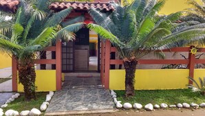 Una entrada de edificio con un camino de baldosas, un portón de madera y dos palmeras.