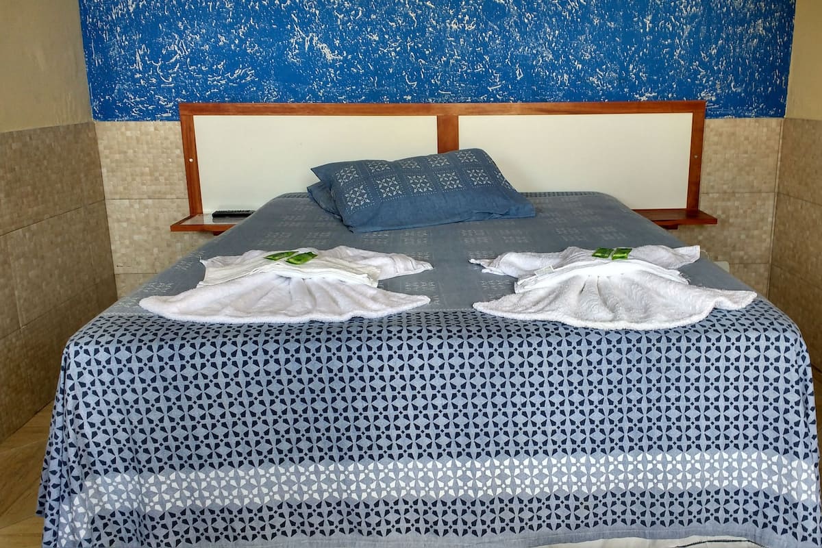 Una cama bien hecha con un edredón estampado, dos toallas y una almohada azul.