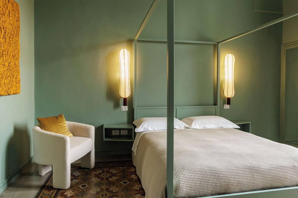 A four-poster bed with a green wall and patterned floor tiles.