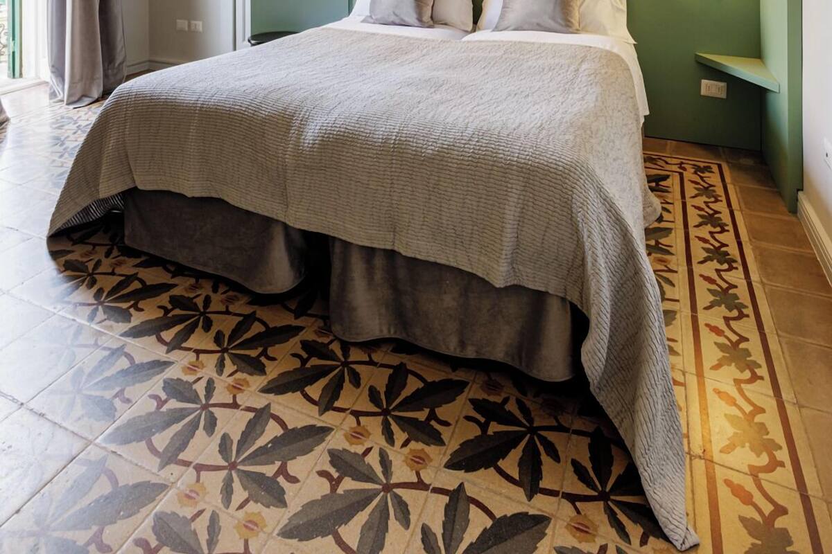 A hotel room with a large bed, a green accent wall, and a patterned floor.