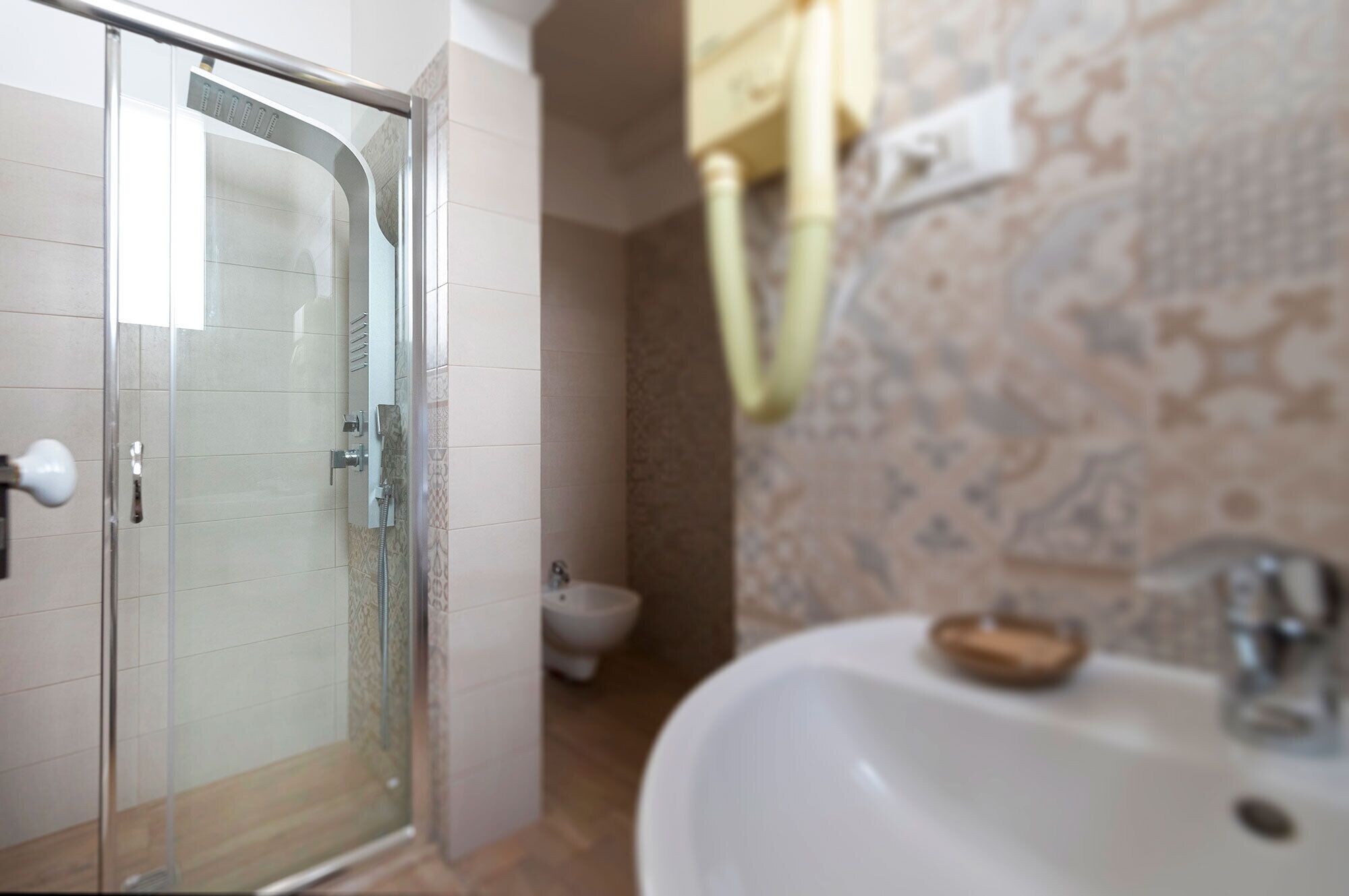 Un baño con cabina de ducha de vidrio, inodoro y lavamanos con jabonera.