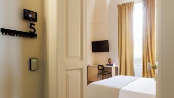 Habitación de hotel con cama, escritorio, silla, televisor y cámara en la pared.
