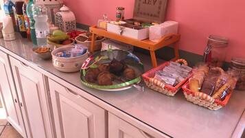A kitchen counter with various food items and kitchenware, including a basket of croissants, a bowl of snacks, and several bottles of beverages.