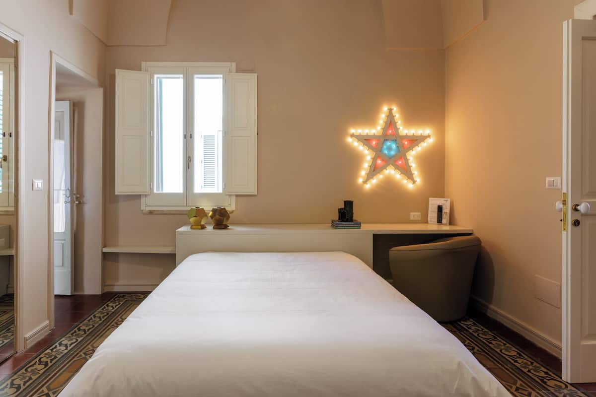 A bedroom with a bed, a desk, a chair, a star-shaped light fixture, and a window with shutters.