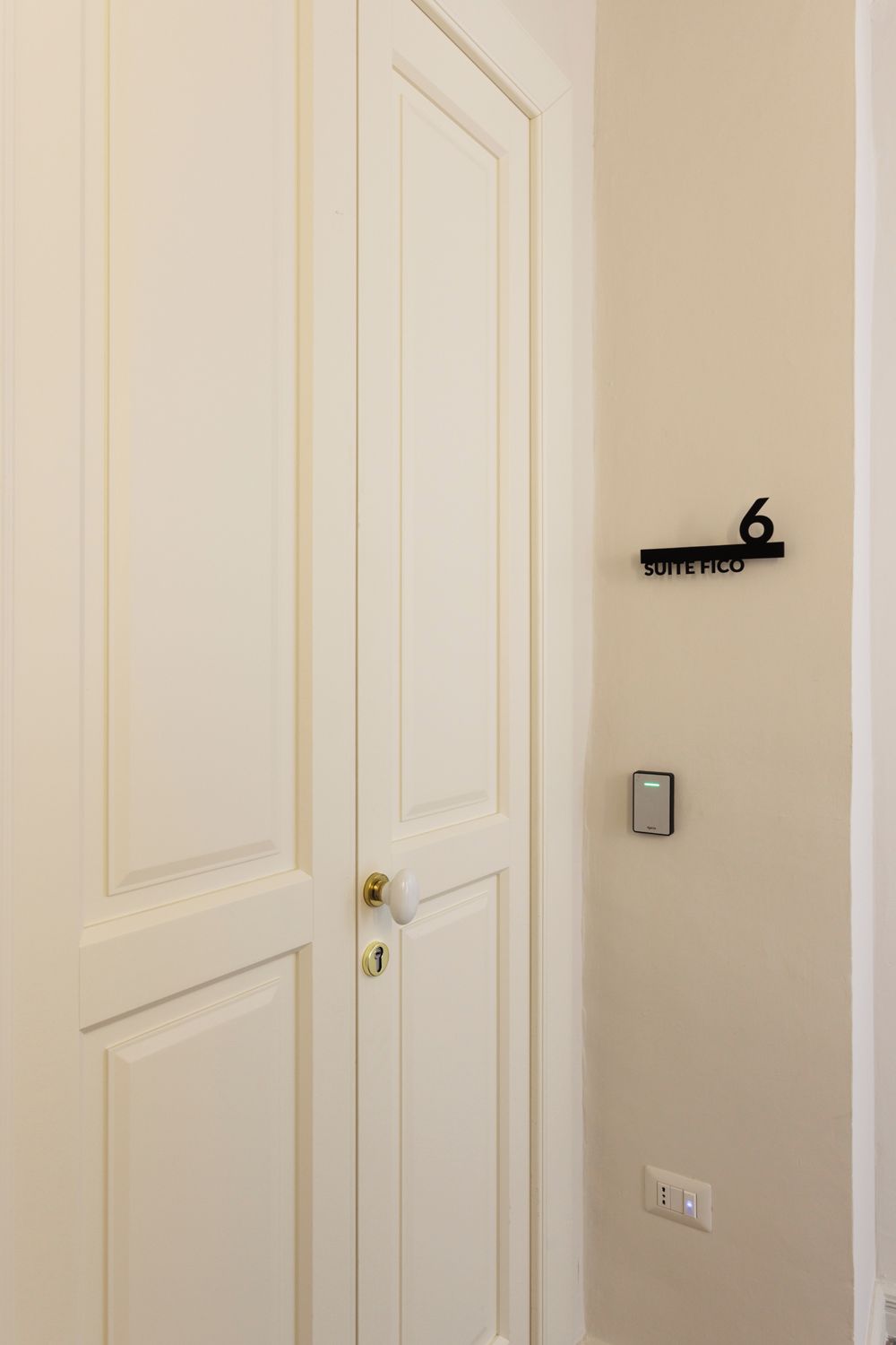 Una puerta blanca con una cerradura y un ojo de cerradura. Un letrero negro con el número 6 y la inscripción 