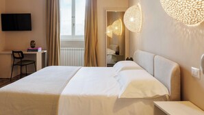 Ein Hotelzimmer mit einem großen Bett, einem Schreibtisch mit Stuhl, einem an der Wand montierten Fernseher und einem großen Fenster mit Vorhängen.