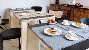 Ein Essbereich mit einem langen Tisch, gedeckt für vier Personen, umgeben von Stühlen. Über dem Tisch befinden sich dekorative Wandelemente und eine Vitrine mit Pflanze und Geschirr an der Seite.