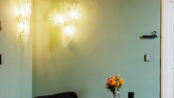 A room with a black sofa, a small round table with a vase of flowers, and wall-mounted lights.