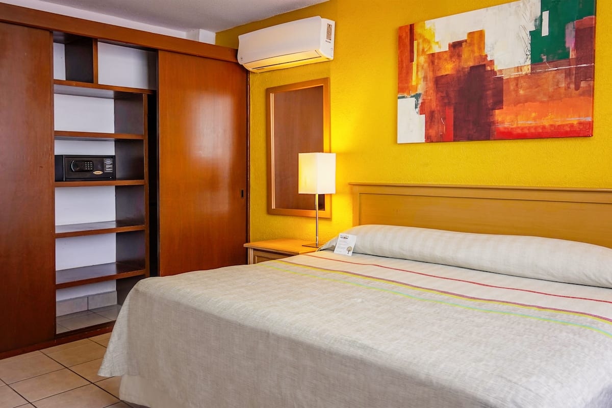 Una habitación de hotel con cama, armario, lámpara de noche y aire acondicionado instalado en la pared.