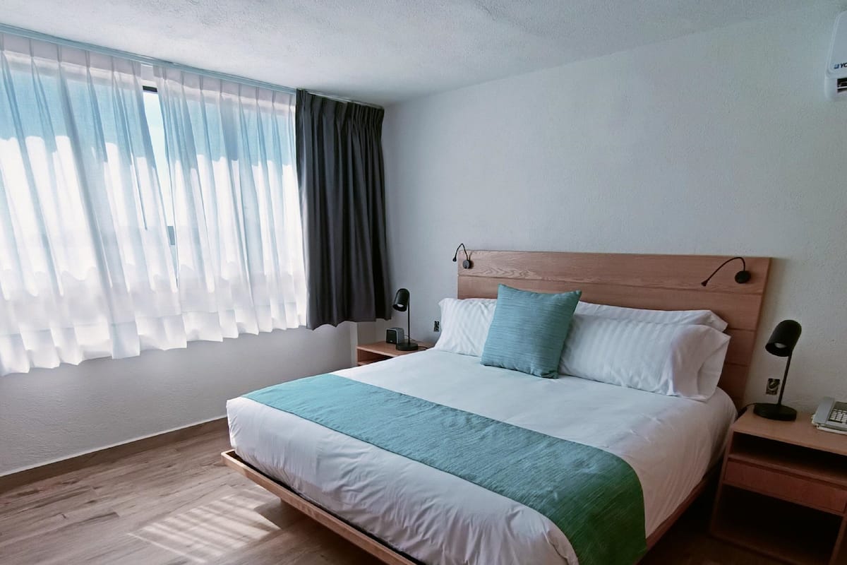 Un dormitorio moderno con estructura de cama de madera, una manta verde y dos mesitas de noche con lámparas.