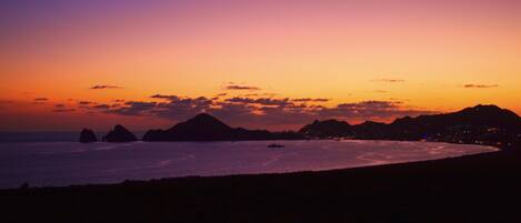 A coastal sunset with silhouettes of mountains and a beach.