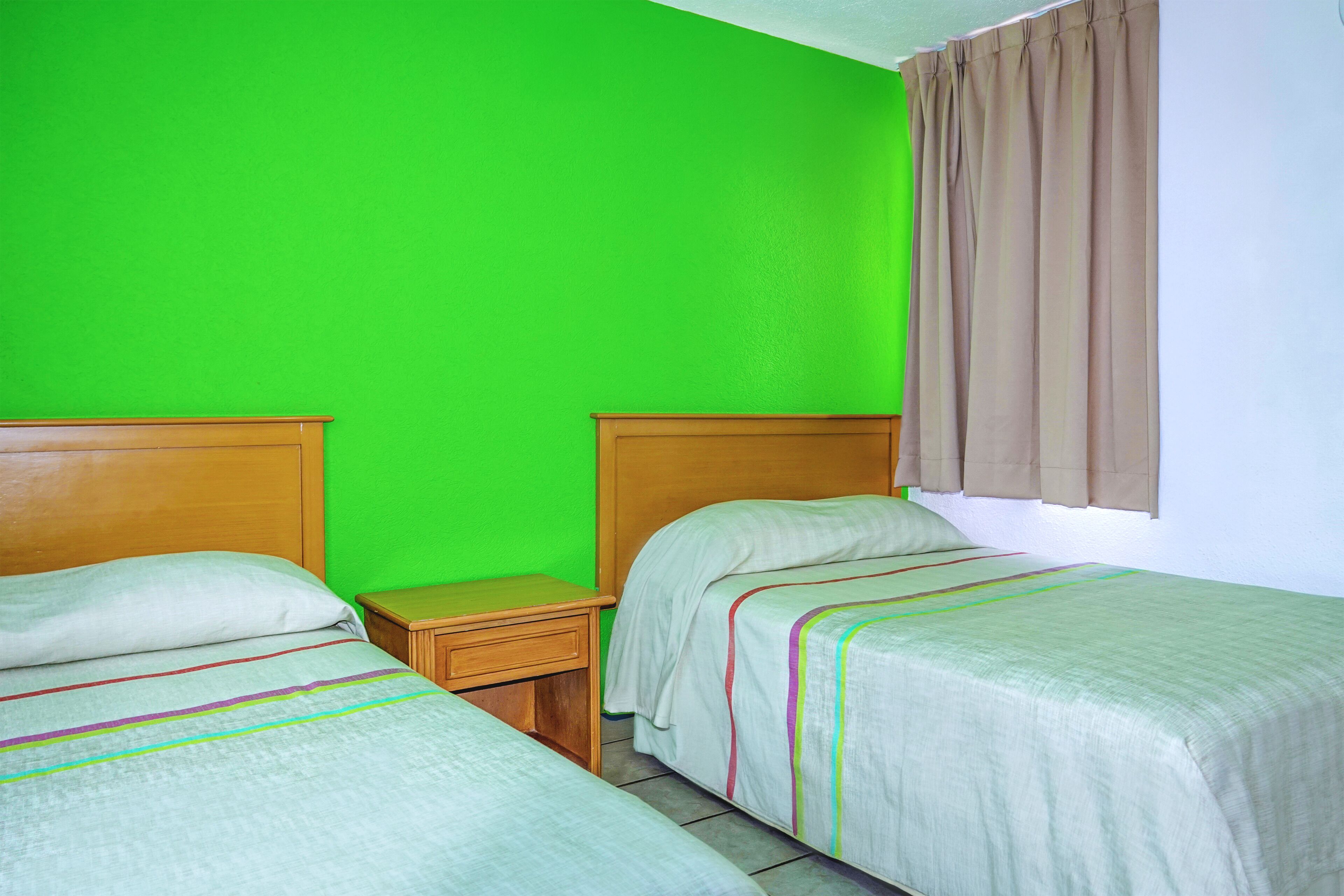A room with two beds, a nightstand, and a window with curtains.