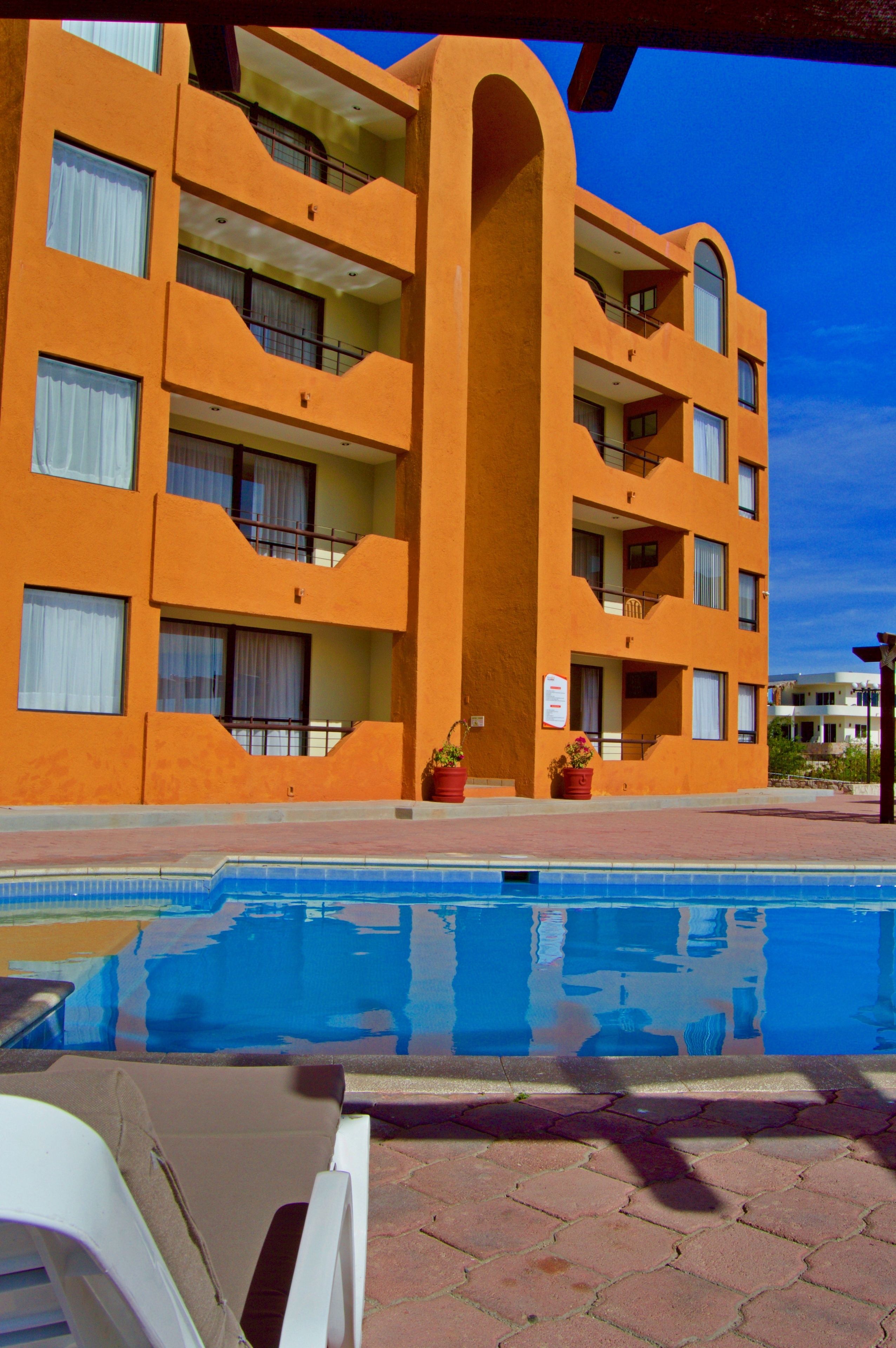 Et hotel med flere etager, altaner, en swimmingpool og plantekasser.