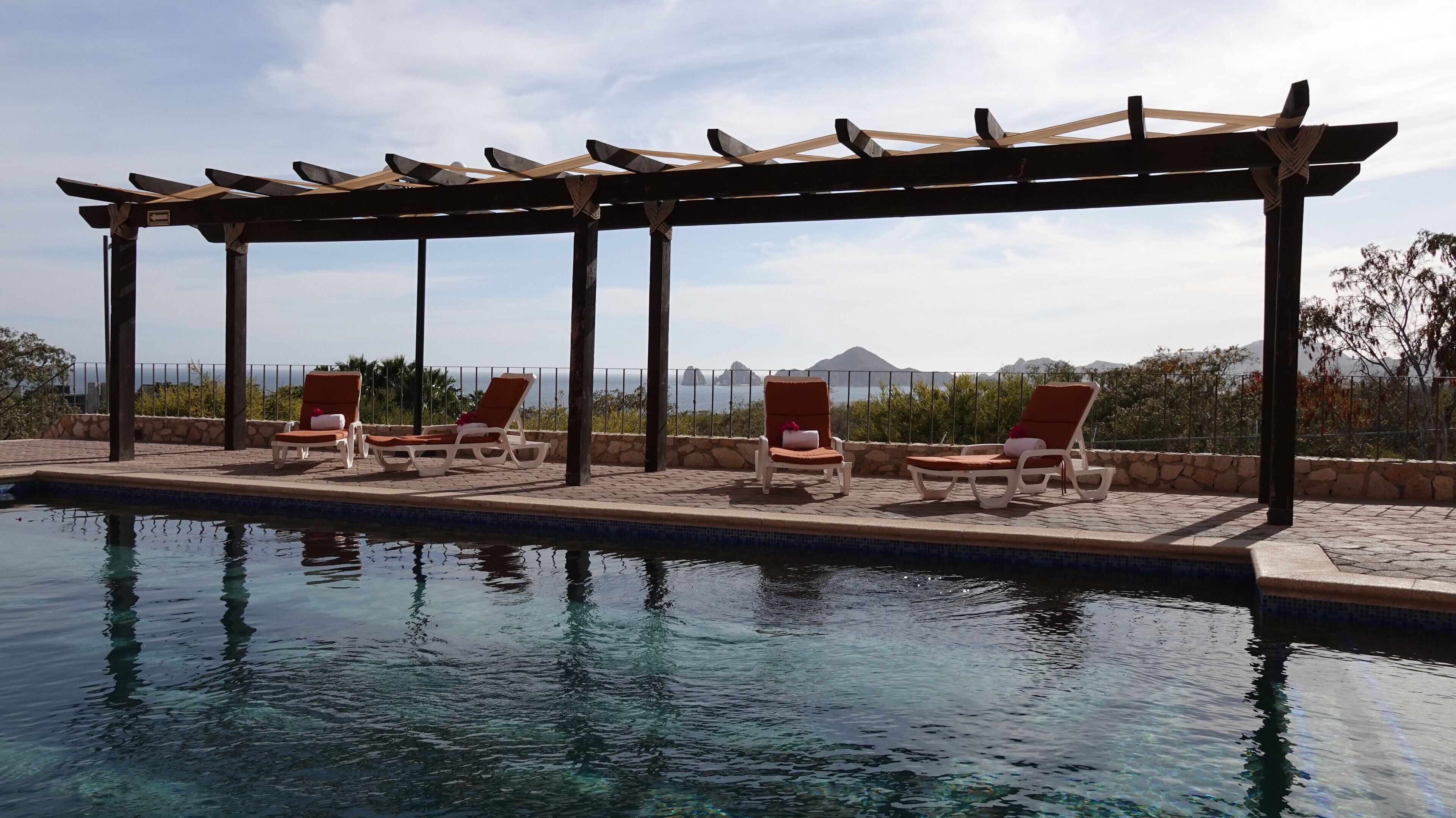 Een zwembadterras met ligbedden en een pergola.