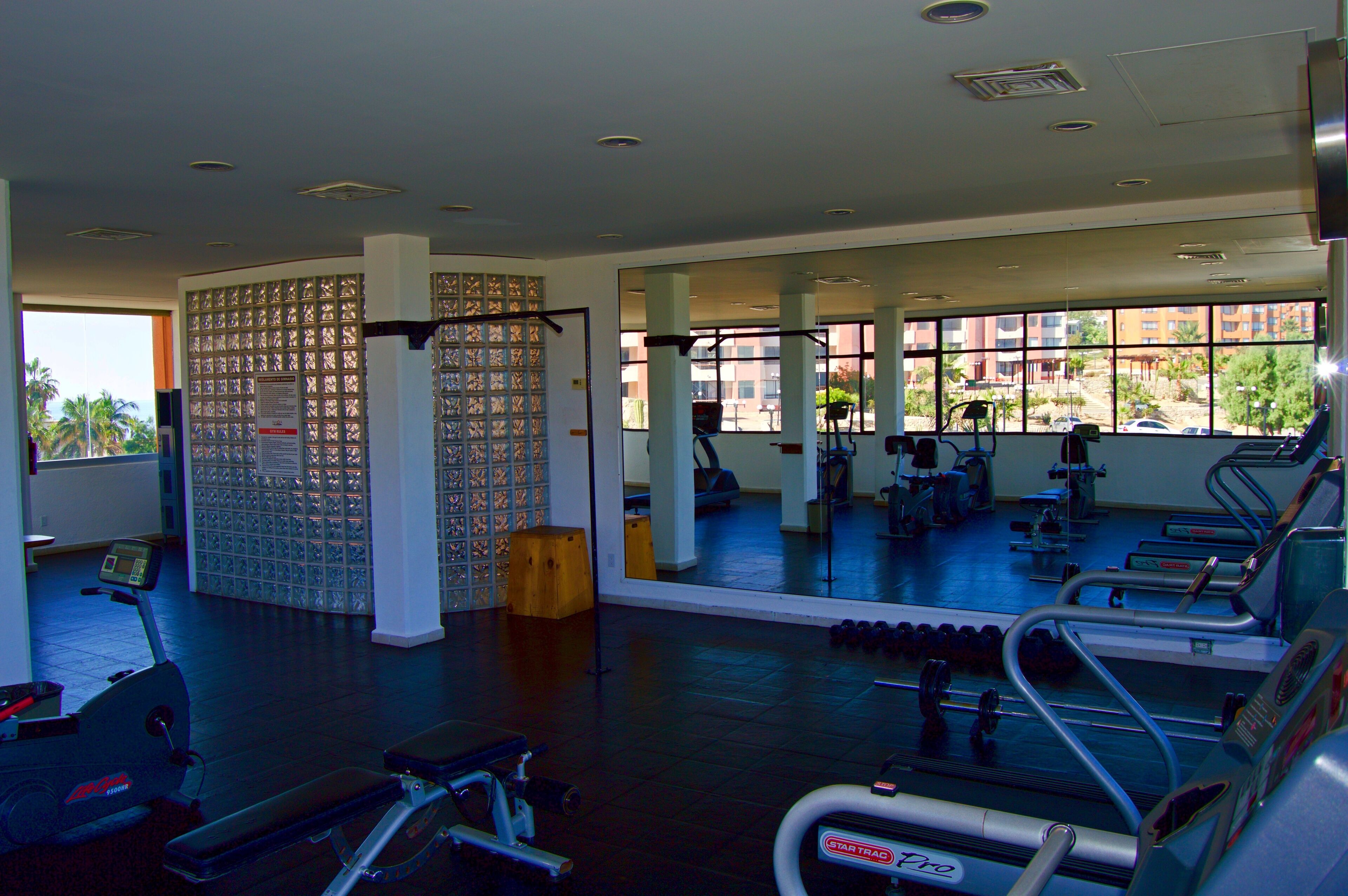 A gym with cardio machines, weights, and a large mirror reflecting the interior.