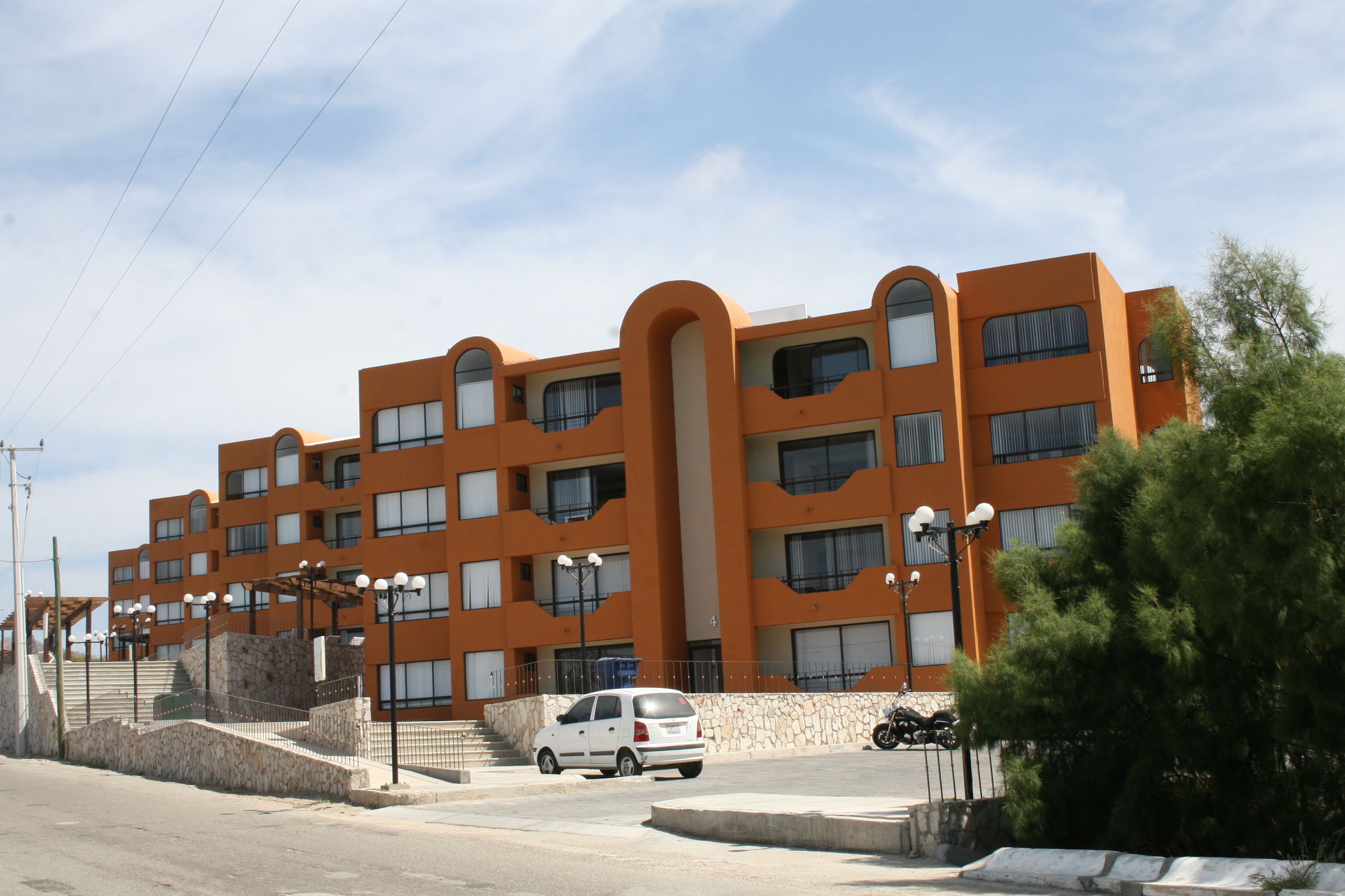 A multi-story orange building with a central staircase, a white car parked in front, and a motorcycle parked to the side.